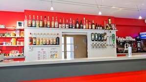 Una zona de bar con estantes llenos de botellas de licores, una máquina de café y una pizarra con el menú.