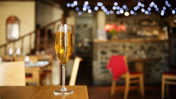 Una copa de vino sobre una mesa de madera en un restaurante con una barra al fondo.