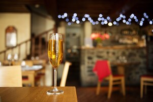 Una copa de vino sobre una mesa de madera en un restaurante con una barra al fondo.