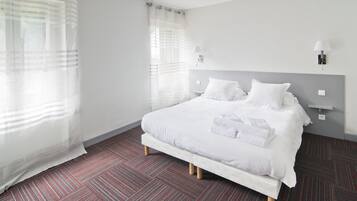 Una habitación de hotel con una cama grande, ropa de cama blanca y alfombra a rayas.