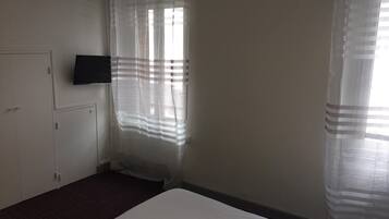 A room with a bed, a television mounted on the wall, and a window with sheer curtains.
