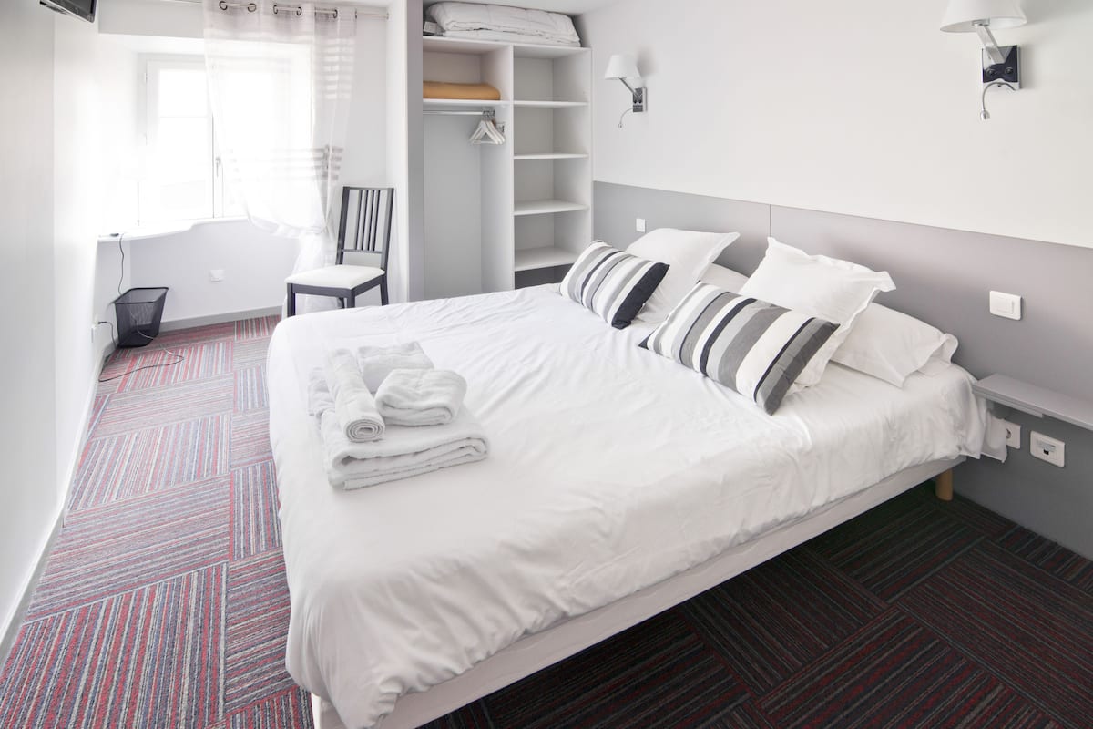 Une chambre d’hôtel avec un grand lit, un dressing, une chaise et une salle de bain avec baignoire.