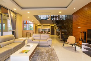 Uma sala de estar moderna com sofá, poltrona e mesa de centro. Uma escada leva a um andar superior.