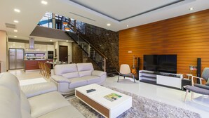 Una sala de estar moderna con un sofá blanco, una mesa de centro y un televisor. Se ve una escalera que conduce a un nivel superior.