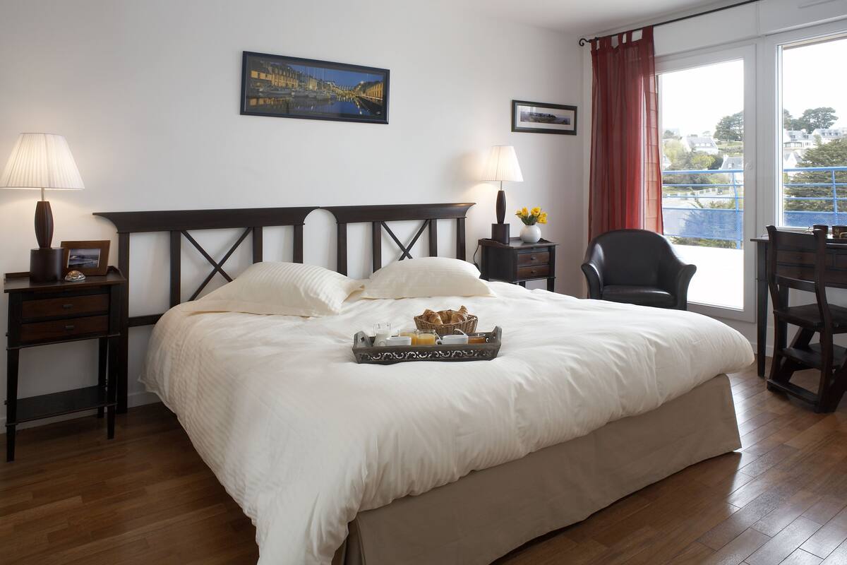 Una cama bien hecha con una bandeja de desayuno, una silla, un escritorio y una ventana con vistas.