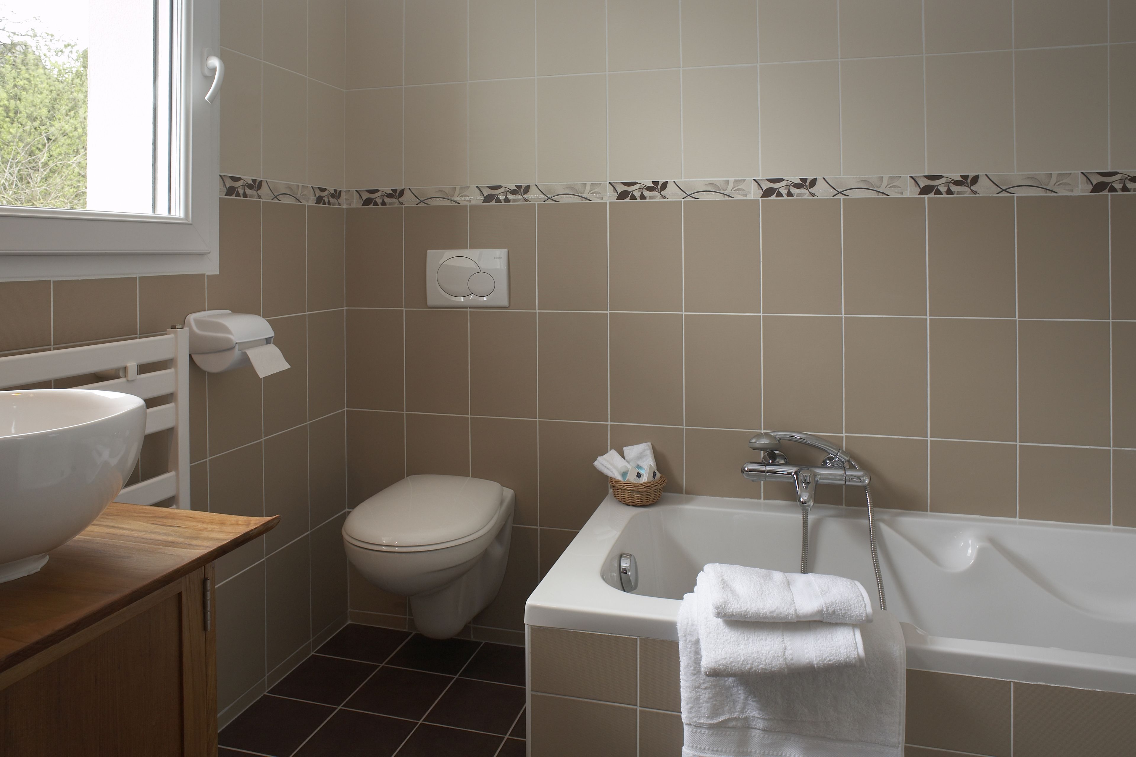 A bathroom with a large white bathtub, a wooden vanity with a white sink, a toilet, and a window.