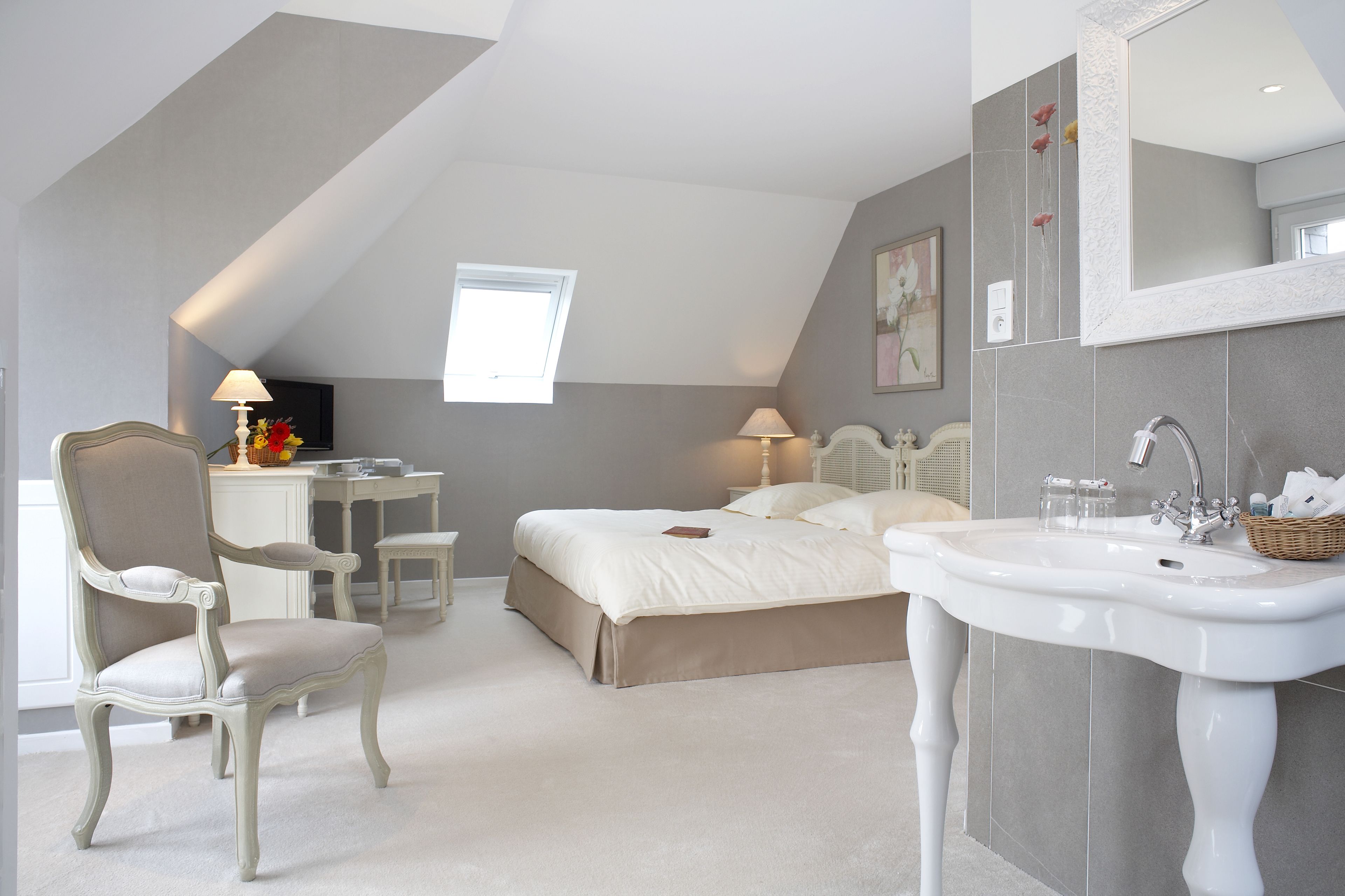 A bedroom with a large bed, a desk, a chair, a vanity with a sink, and a window.