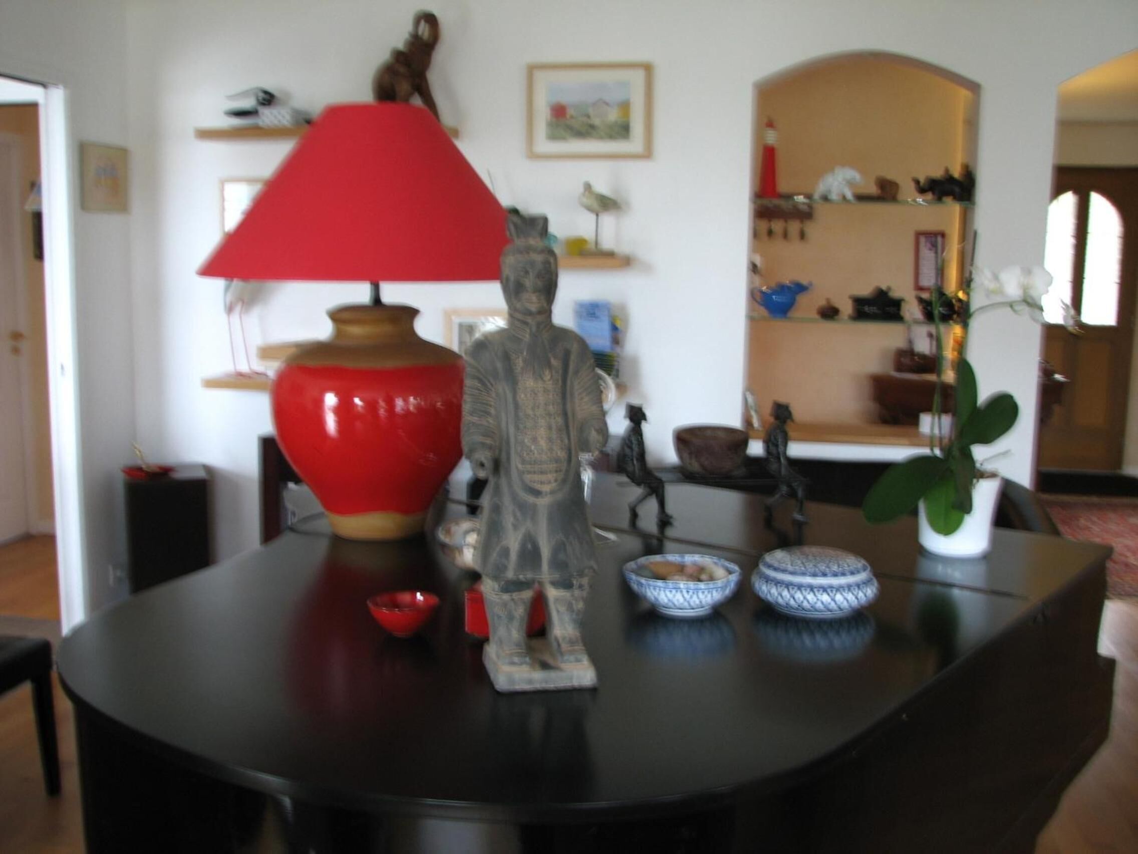 Une table à manger avec une lampe rouge, un vase et une statue. Il y a deux bols sur la table.