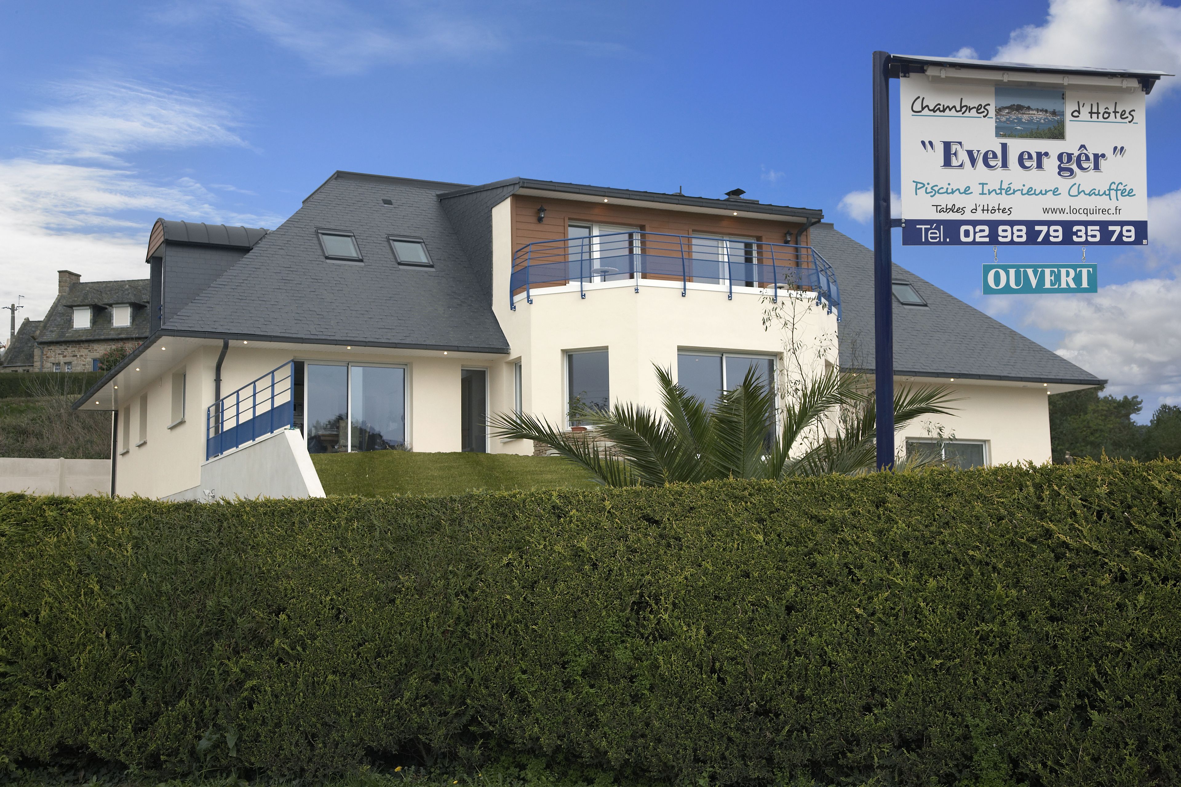A modern two-story house with a balcony, a swimming pool, and a sign advertising a hotel.