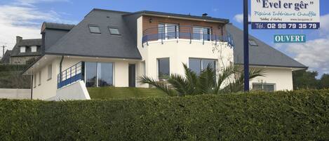 A modern two-story house with a balcony, a swimming pool, and a sign advertising a hotel.