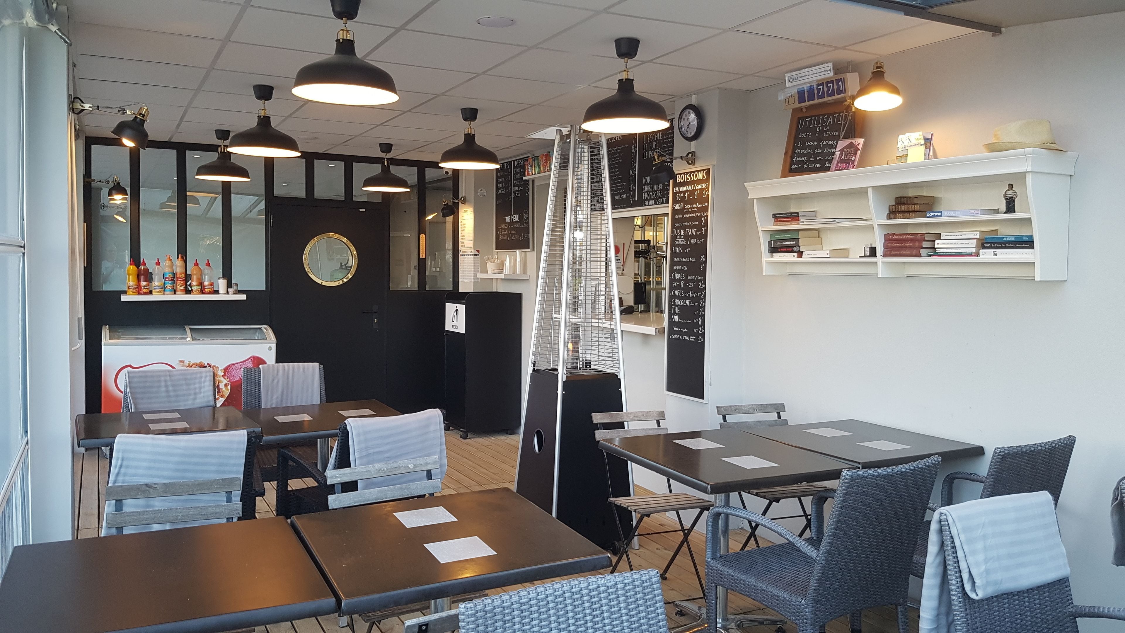 Un café avec des tables et des chaises, un tableau affichant le menu et une horloge au mur.