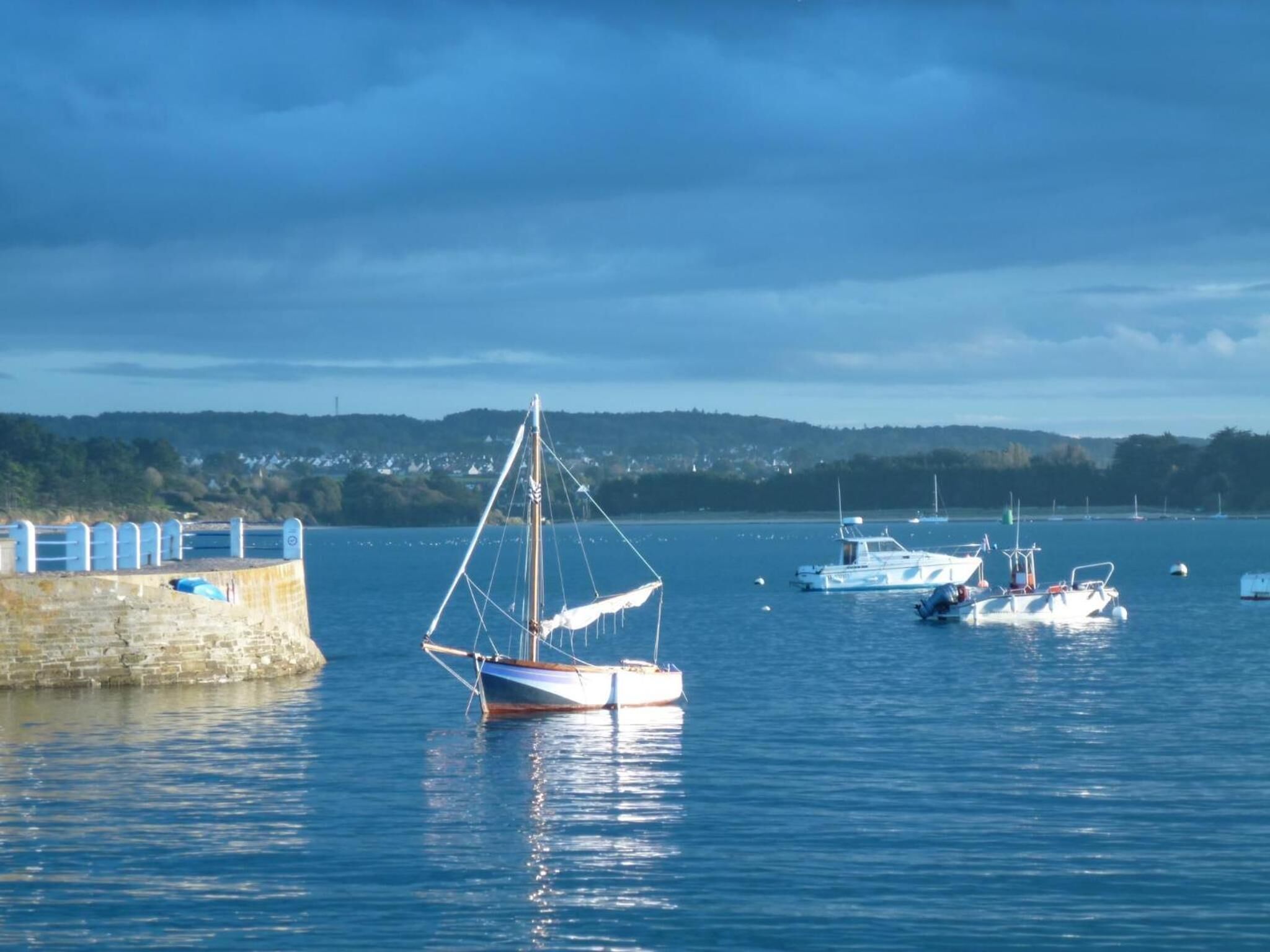 A harbor with boats docked, a stone wall, and a distant shoreline with buildings.