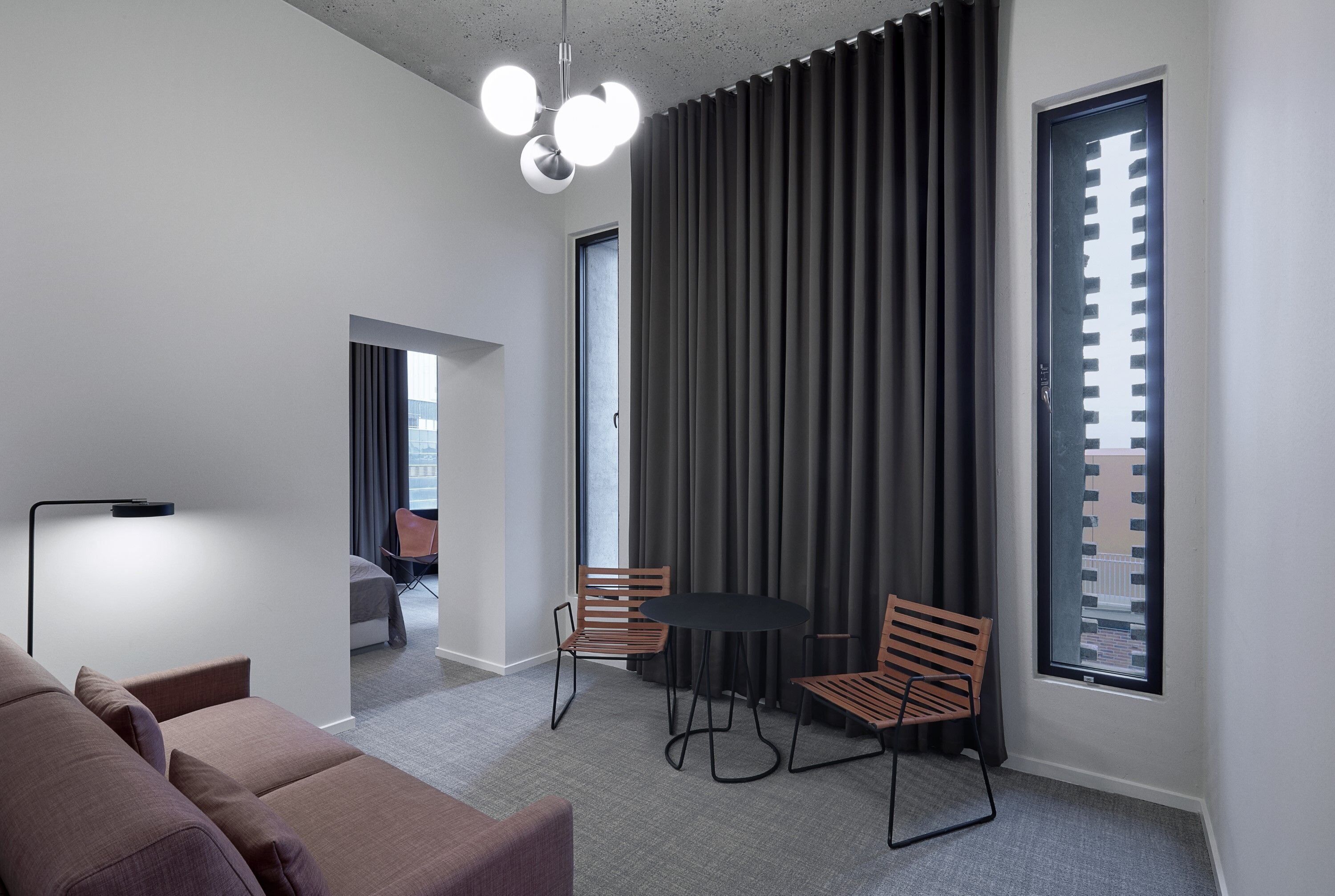 A modern room with a sofa, a table with two chairs, a floor lamp, and a large window with blinds.