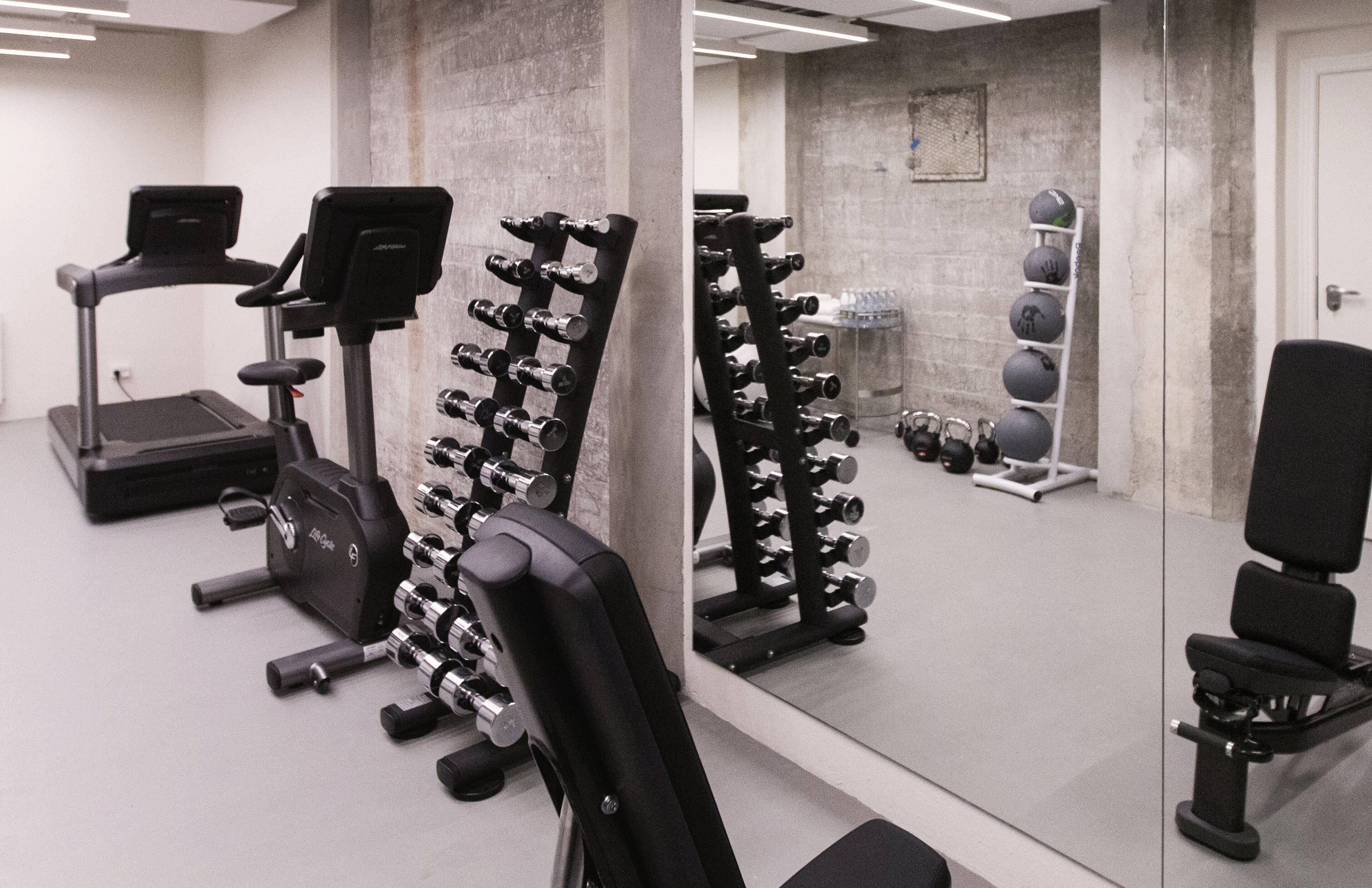 Et fitnessrum med træningsudstyr, løbebånd og spejlvæg.
