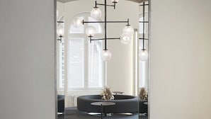Un intérieur moderne avec un parquet en chevrons, un canapé foncé, une chaise en bois et une cloison en verre agrémentée de luminaires suspendus.