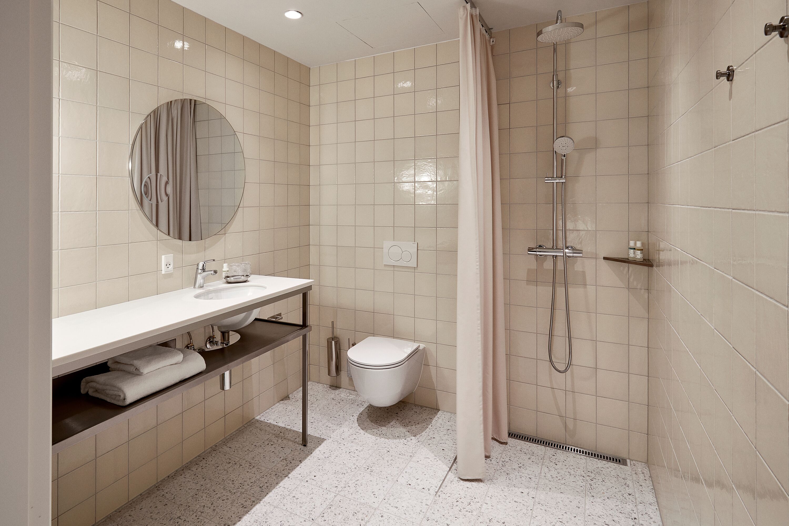 Un baño moderno con un espejo redondo, un lavamanos, un inodoro y una zona de ducha.