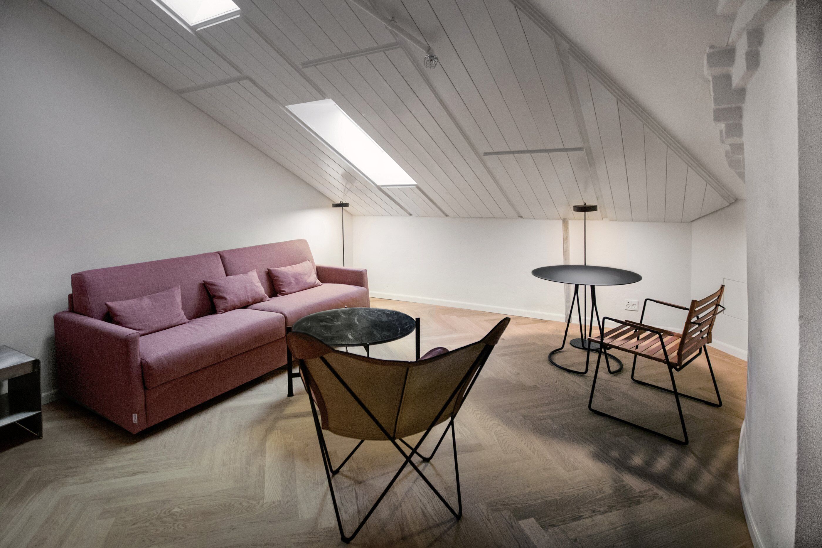 A modern loft apartment with a high ceiling, wooden flooring, a pink sofa, a round table, and two chairs.