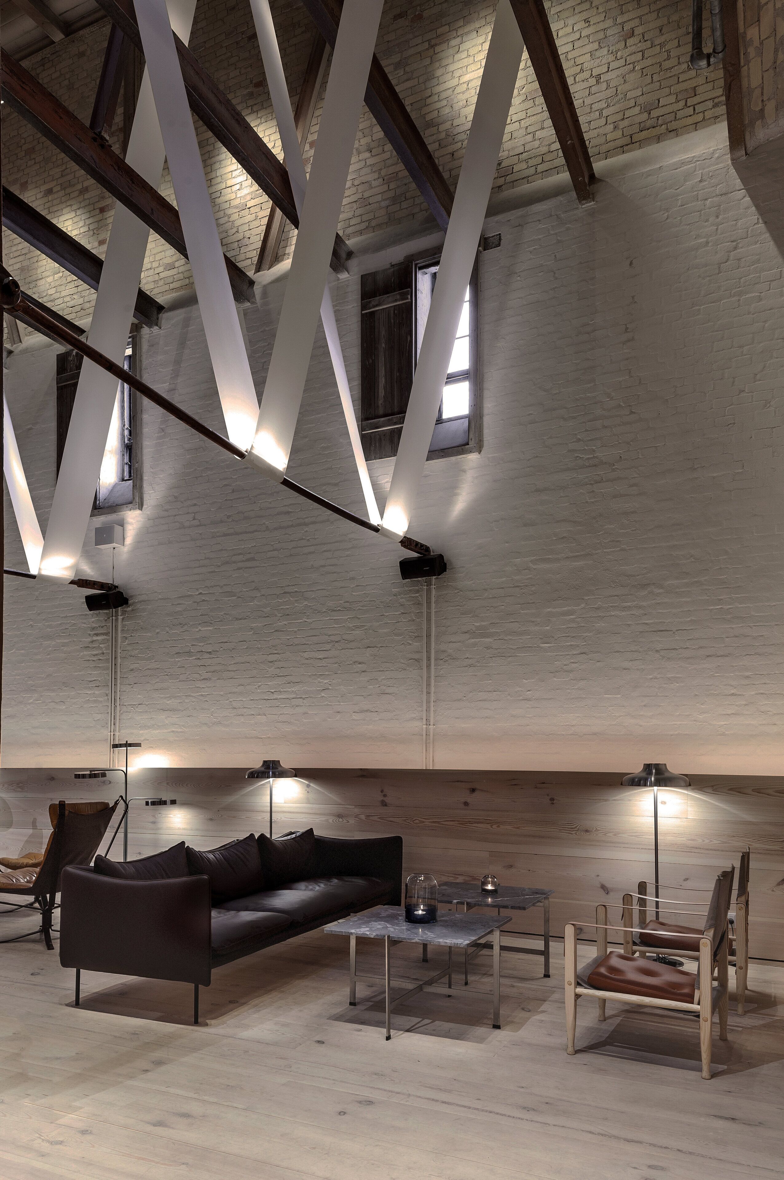 A loft-style room with exposed brick walls, a sloped ceiling with wooden beams, a black leather sofa, a coffee table, and two chairs.