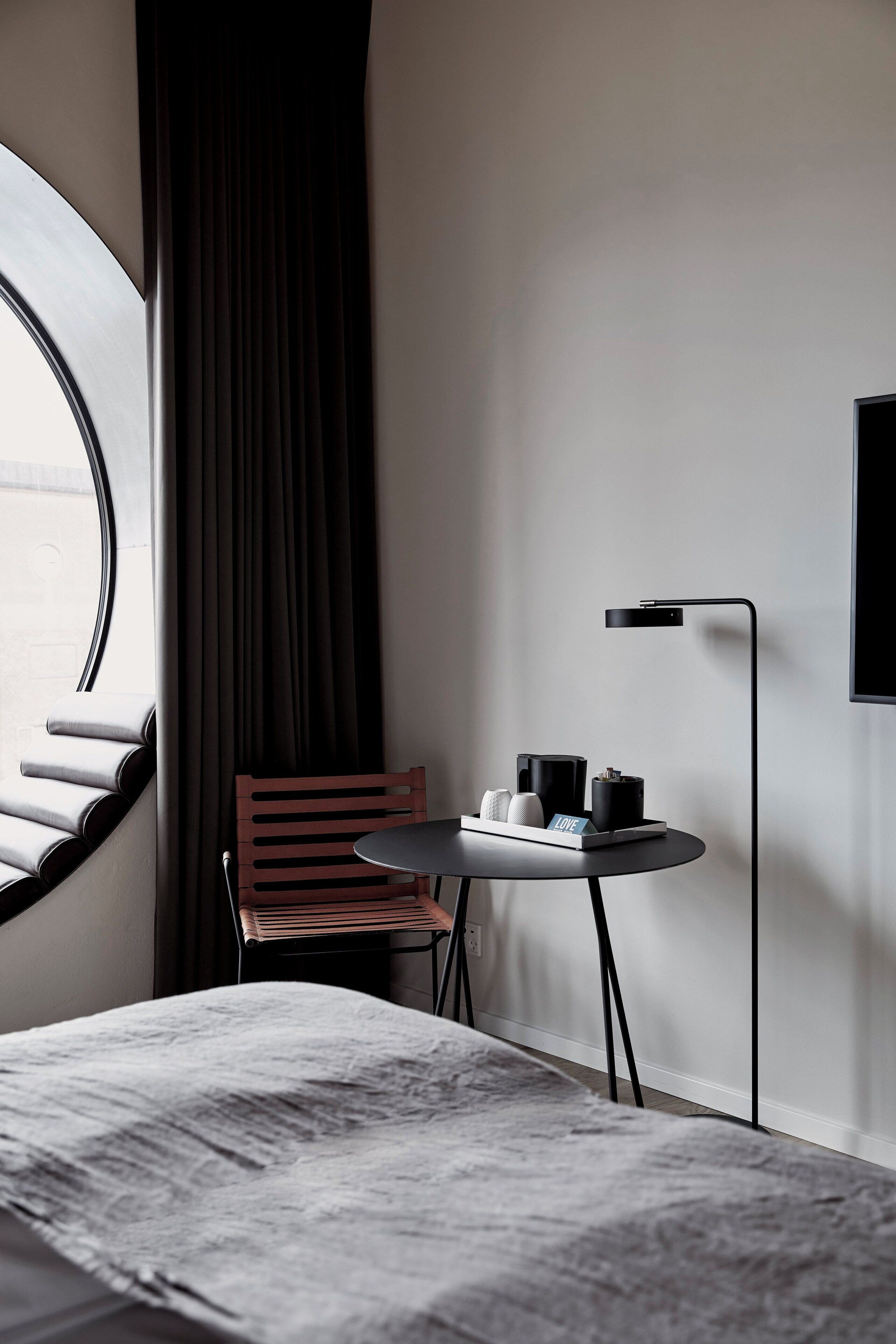 Una habitación de hotel moderna con una cama, una mesita con una silla, un televisor y una ventana con cortinas.