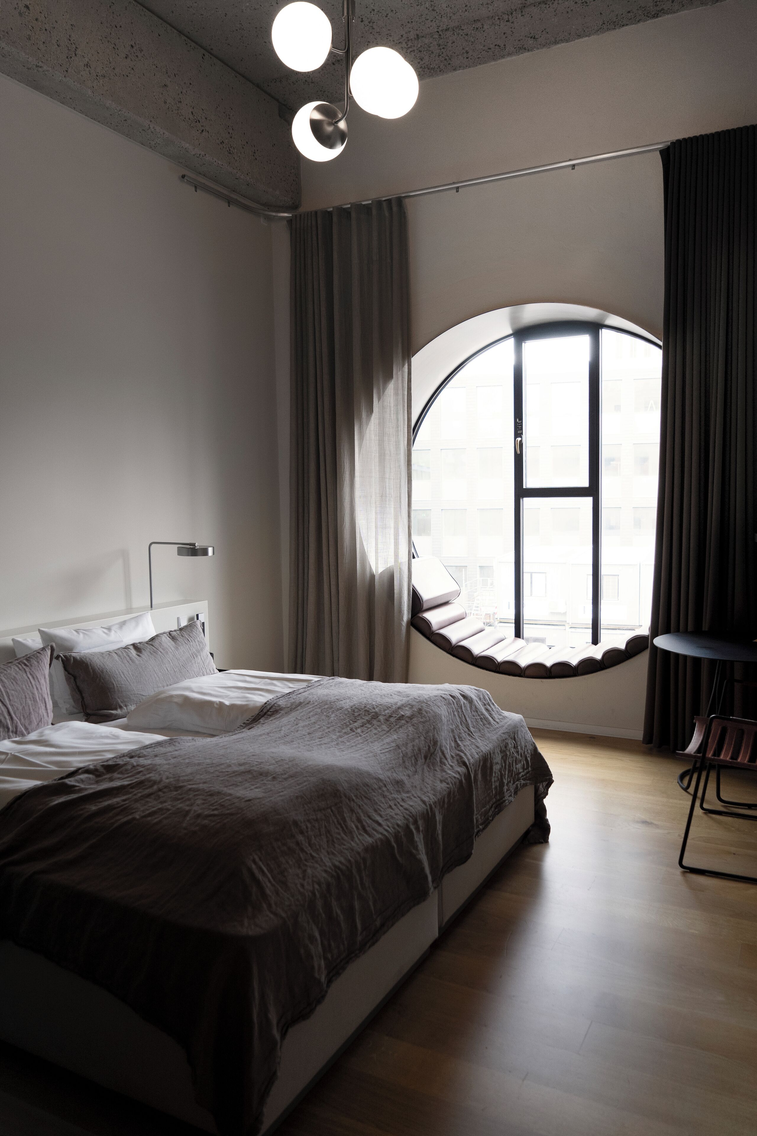 Quarto moderno com uma cama grande, uma janela redonda e um lustre.