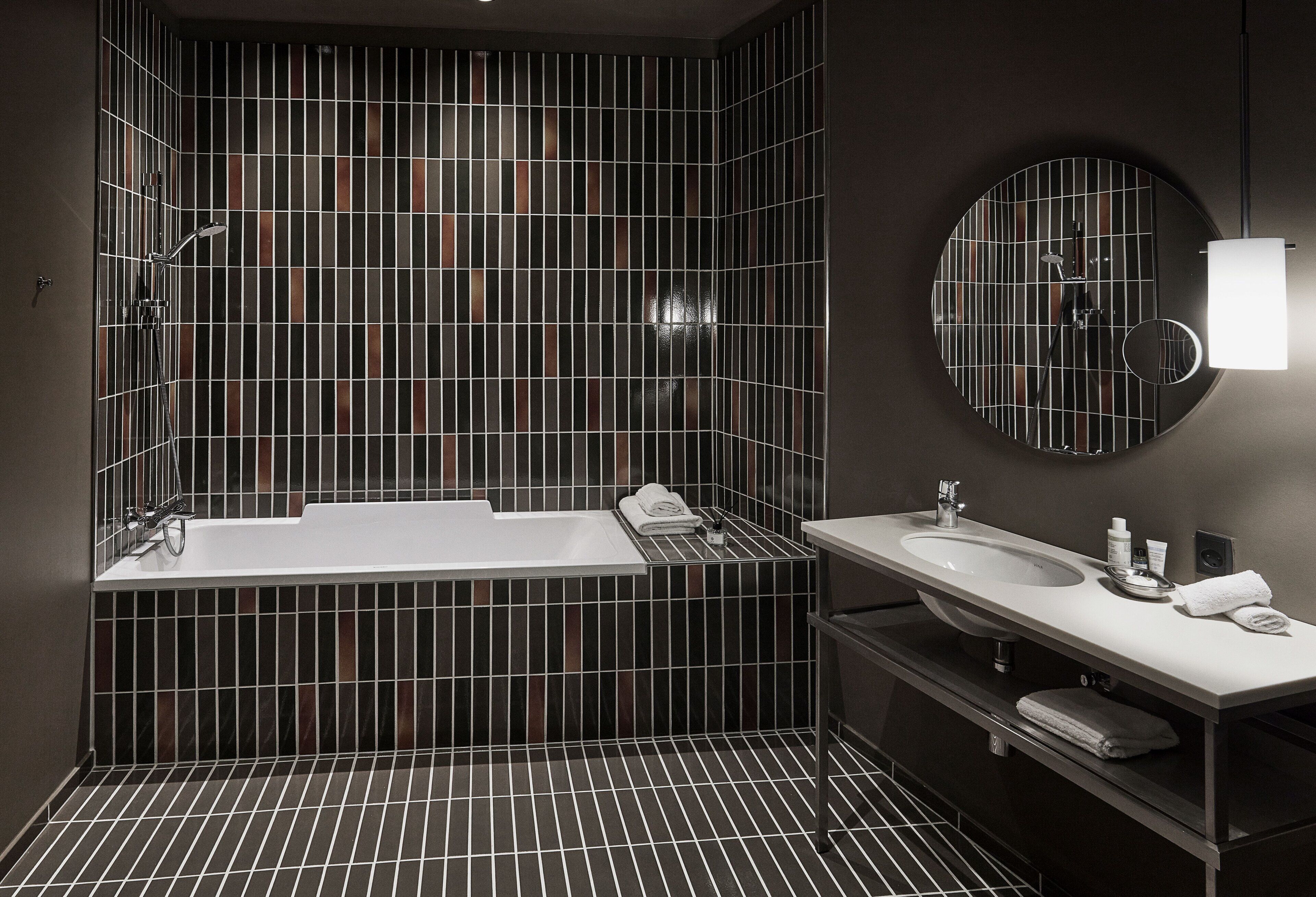 Une salle de bain moderne avec une grande baignoire, un meuble-lavabo à deux vasques et un miroir doté d’un cadre circulaire.