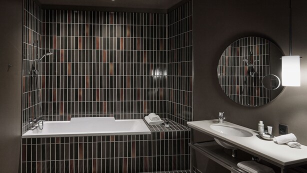 A modern bathroom with a large bathtub, a double sink vanity, and a mirror with a circular frame. - Boutique Hotel Ottilia (Copenhagen)