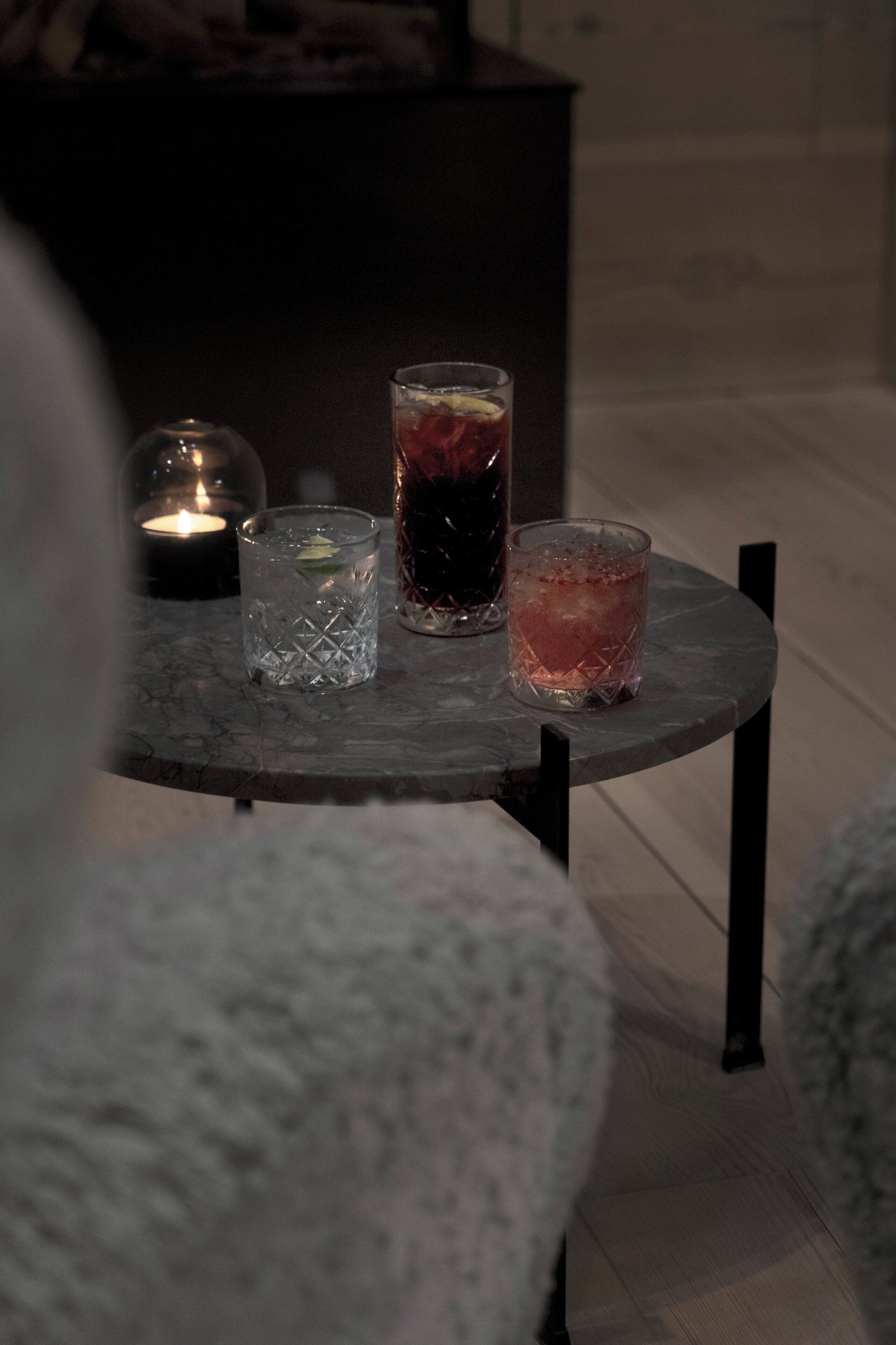 Een marmeren tafel met drie glazen drankjes, een kaars en een glazen stolp.