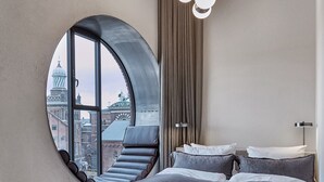 A bedroom with a large circular window, a bed, a chair, and a view of a cityscape. - Boutique Hotel Ottilia (Copenhagen)