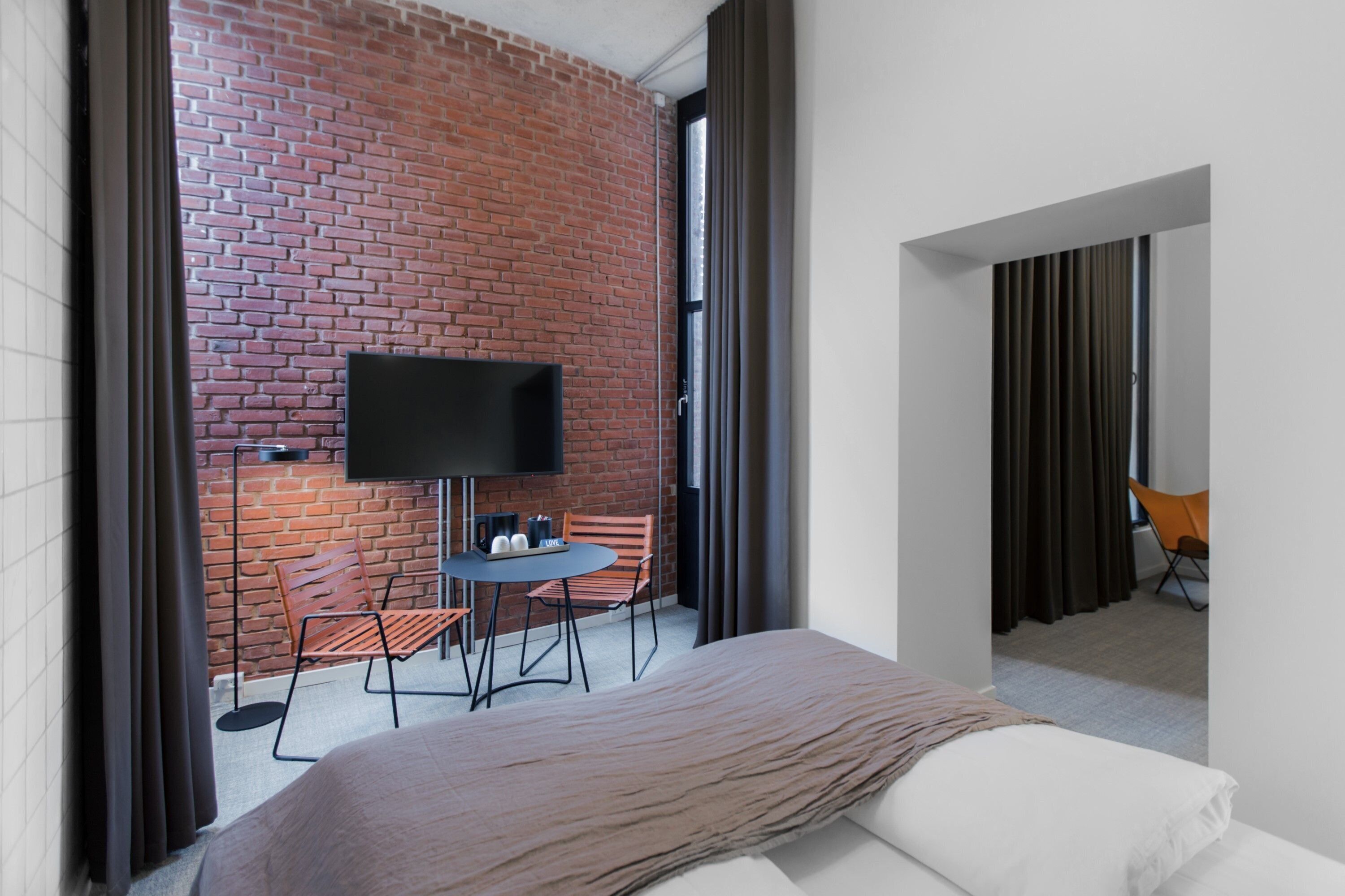 A modern hotel room with a brick wall, a flat-screen TV, a small round table, and two chairs.