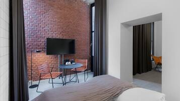A modern hotel room with a brick wall, a flat-screen TV, a small round table, and two chairs.