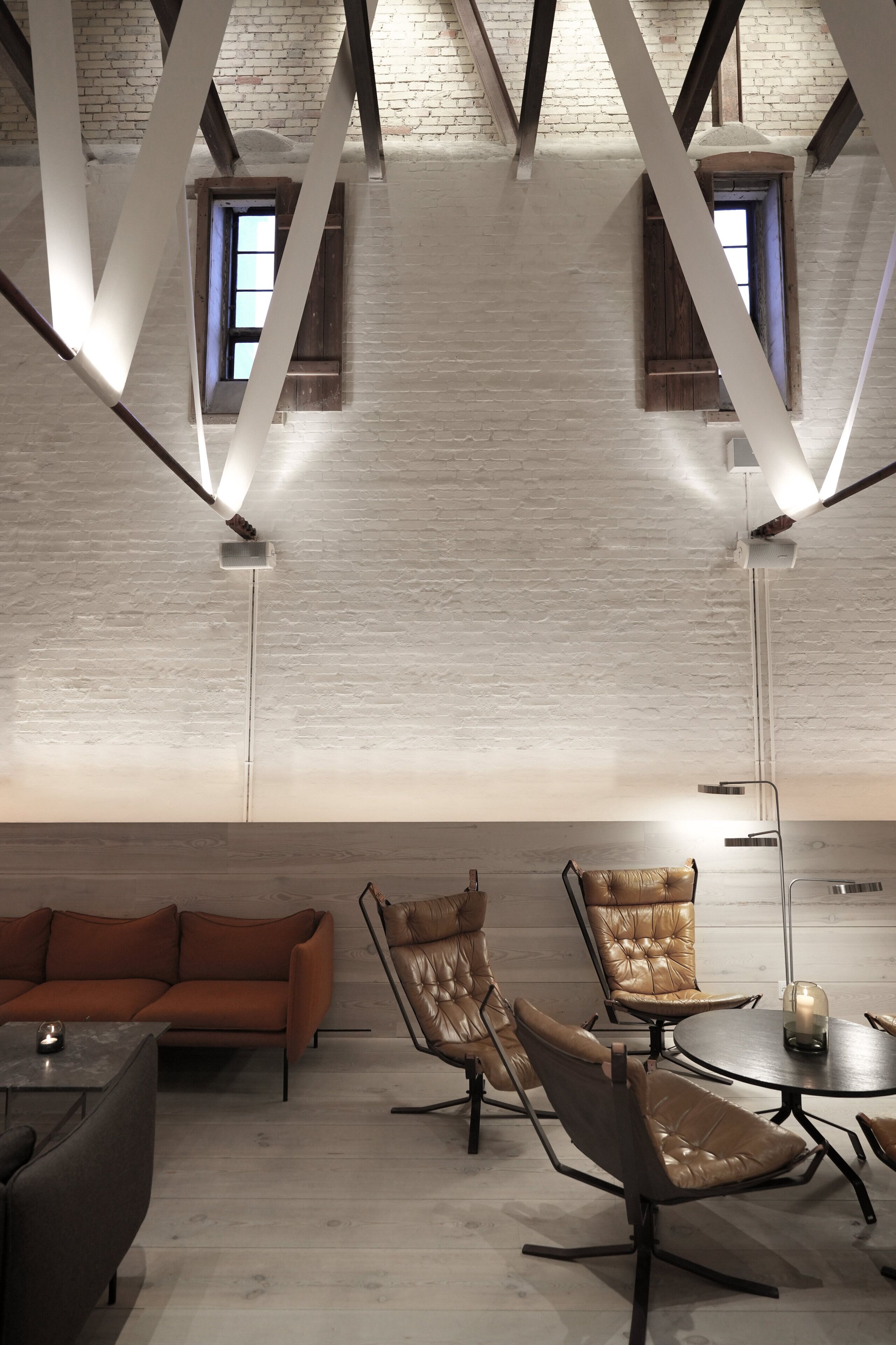 A modern interior with exposed brick walls, a loft-style ceiling, and a mix of seating options including a sofa and leather chairs.