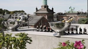 A rooftop terrace with large metal bowls, a building with a green dome, and some greenery in the foreground. - Boutique Hotel Ottilia (Copenhagen)