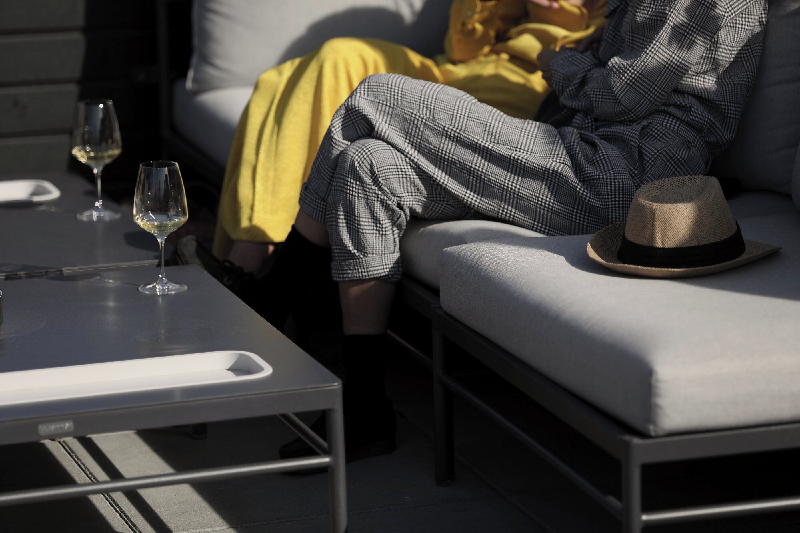 A modern outdoor seating area with a sofa and a table, a hat on the sofa, and two wine glasses on the table.