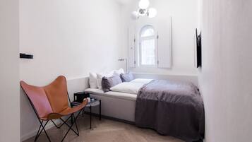 Un dormitorio compacto con cama, una silla, una mesita y una ventana.