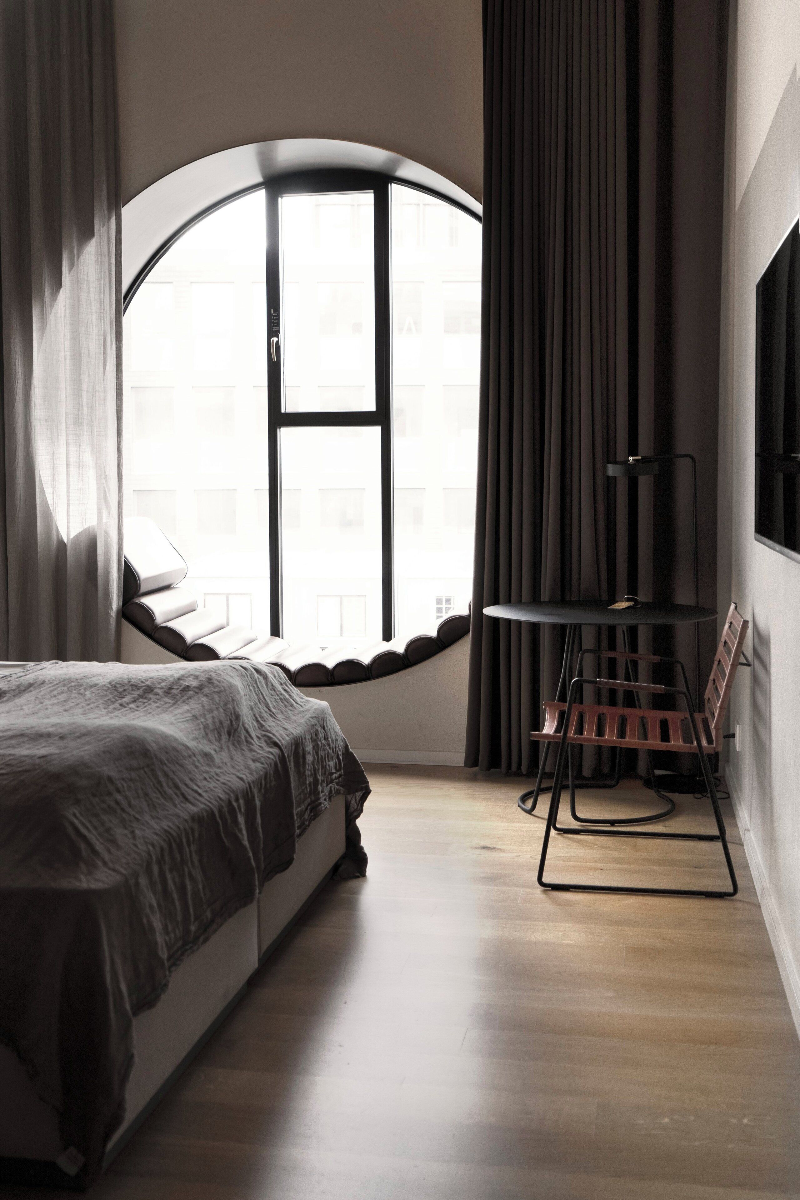 Un dormitorio con una cama, un ventanal redondo, una mesa y una silla.