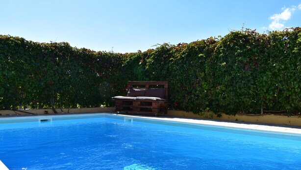 A swimming pool with a wooden deck and a bench in the center. - Helen's Villa (Rafina-Pikermi)
