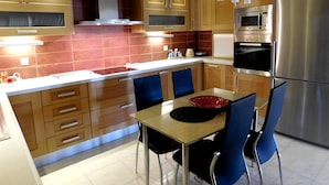 A modern kitchen with wooden cabinets, stainless steel appliances, and a dining area with blue chairs. - Helen's Villa (Rafina-Pikermi)