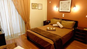 A hotel room with a large bed, a bedside table, a chair, and a window with curtains. - Helen's Villa (Rafina-Pikermi)