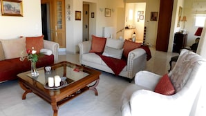 A living room with a sofa, armchairs, a coffee table, and a dining table. There are framed pictures on the walls and a chandelier. - Helen's Villa (Rafina-Pikermi)