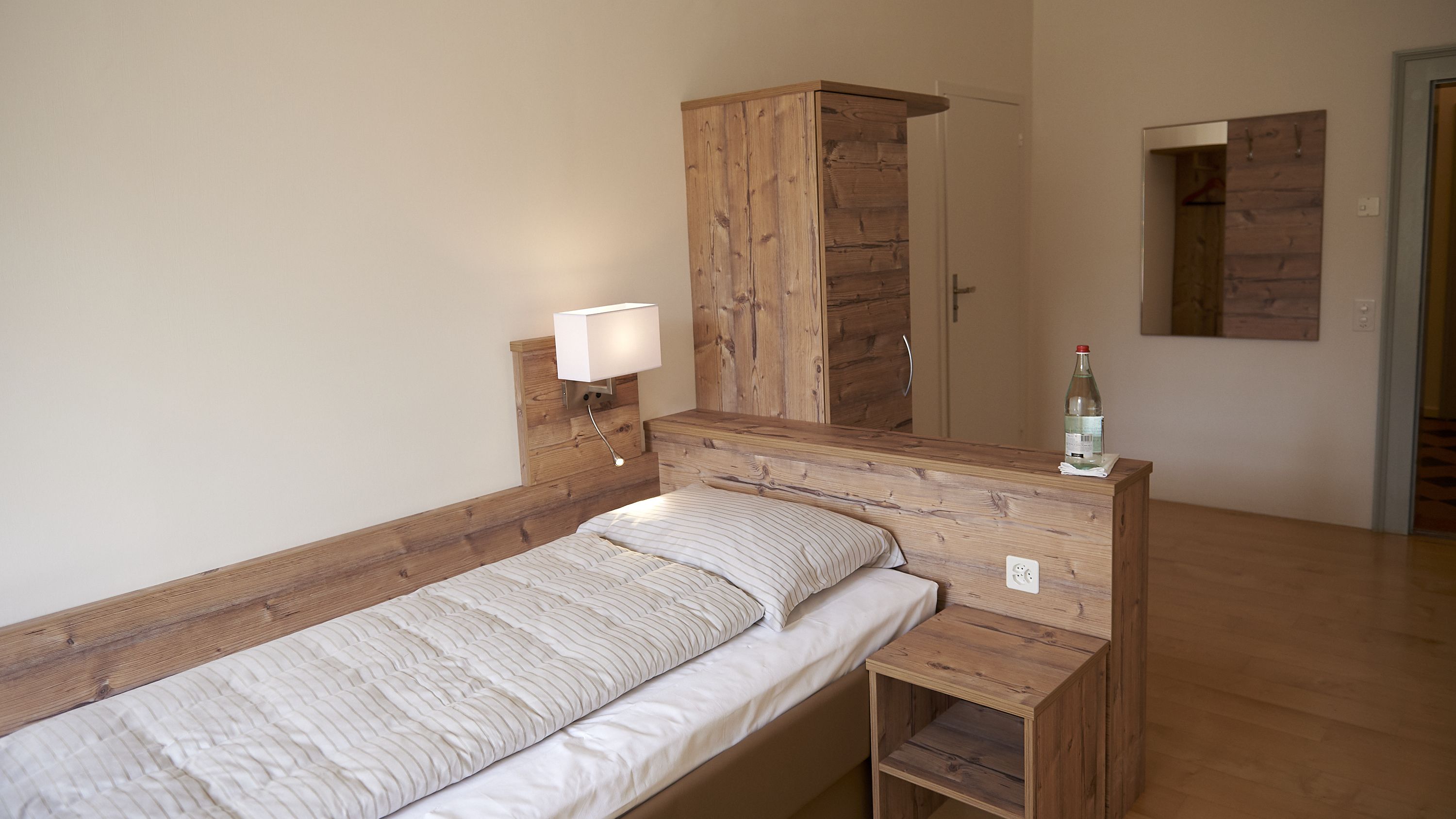 A single bed with a wooden headboard and a nightstand with a lamp.