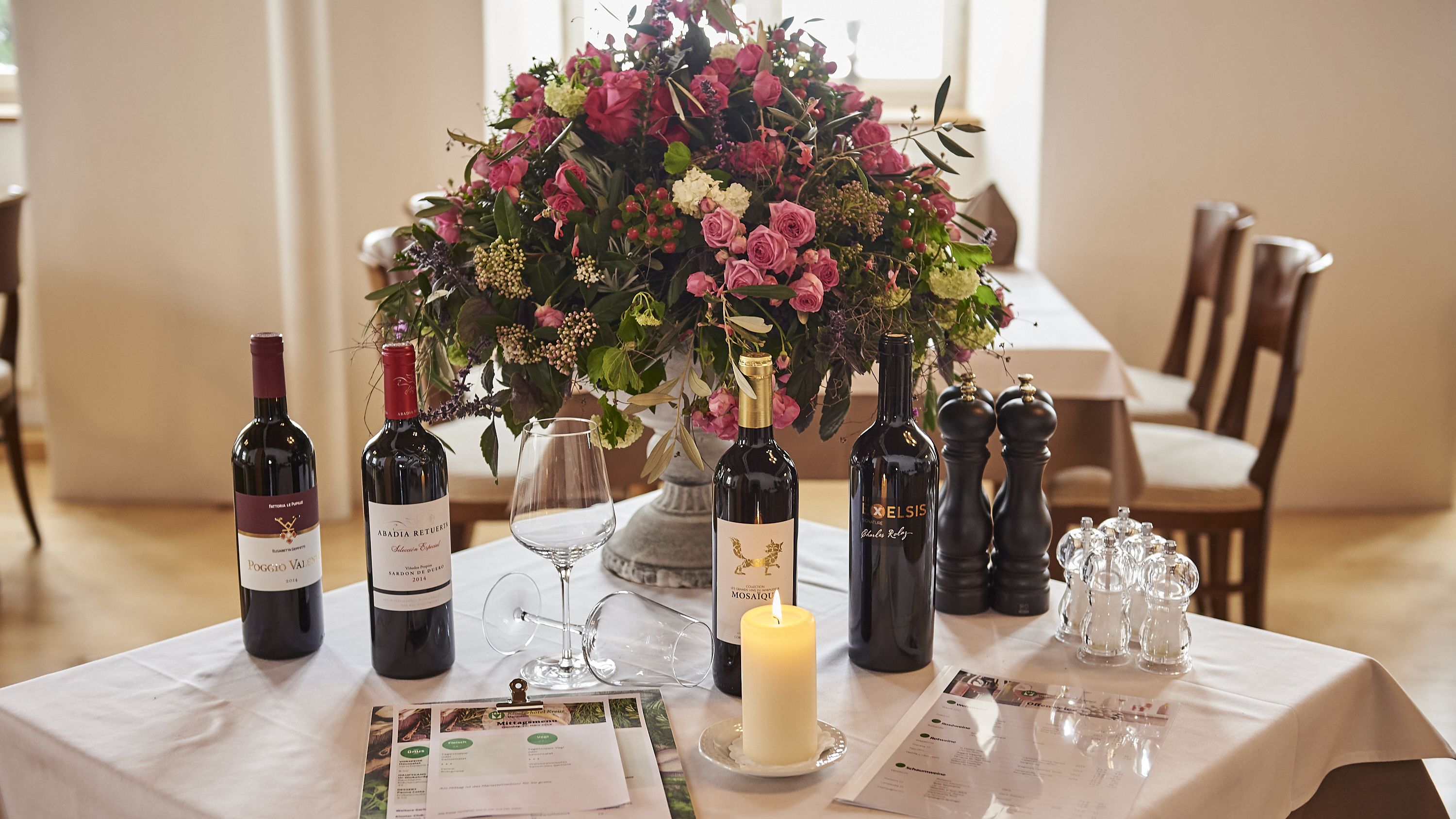 A table set for a meal with wine bottles, a candle, and menus.