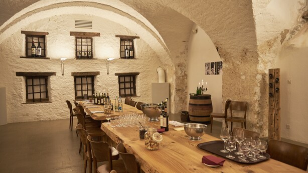A rustic dining room with a long wooden table set for a meal, multiple wine bottles, glasses, and a candle holder. - Klosterhotel Kreuz (Metzerlen)