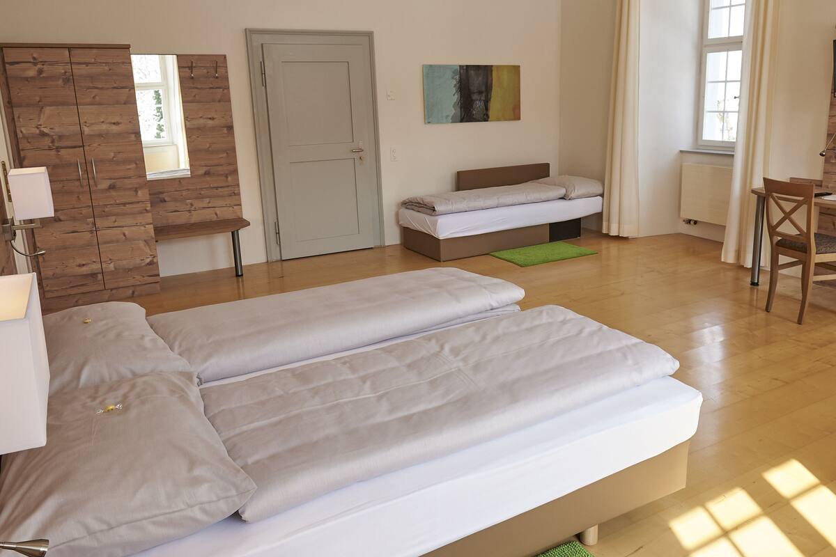 A room with a bed, a desk, a chair, and a television on the wall.