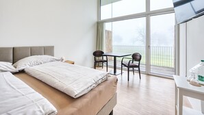 A hotel room with a large bed, a small table with chairs, and a balcony with a view. - Klosterhotel Kreuz (Metzerlen)
