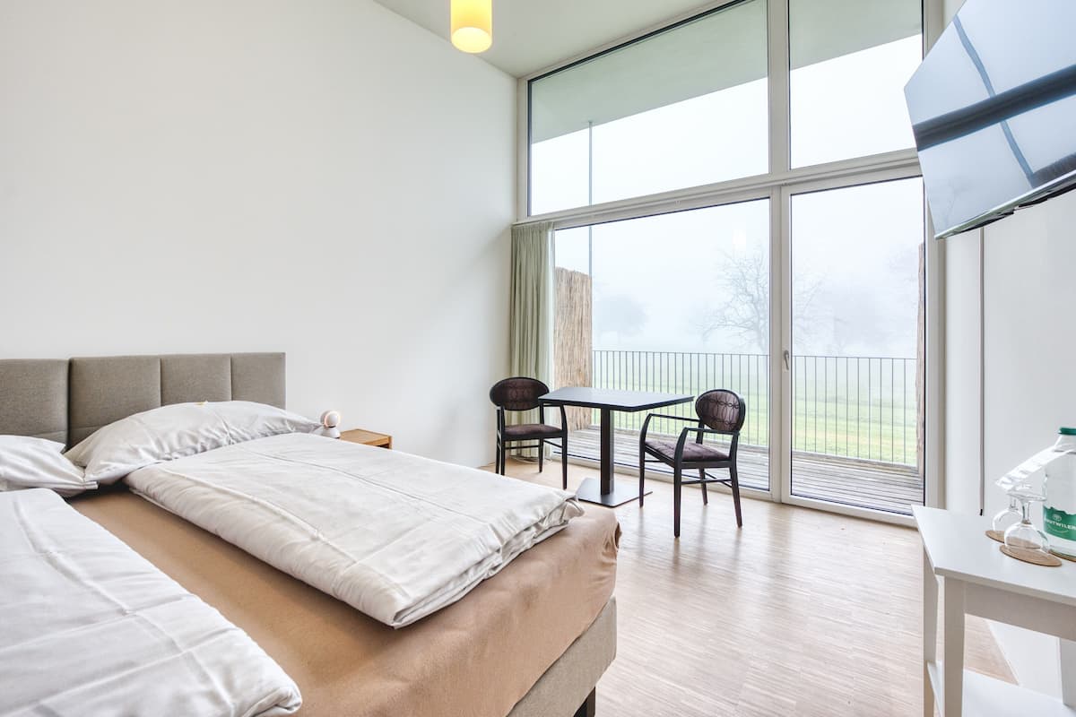 A hotel room with a large bed, a small table with chairs, and a balcony with a view.