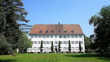 Stately building with a symmetrical facade, surrounded by a well-manicured lawn and tall trees.