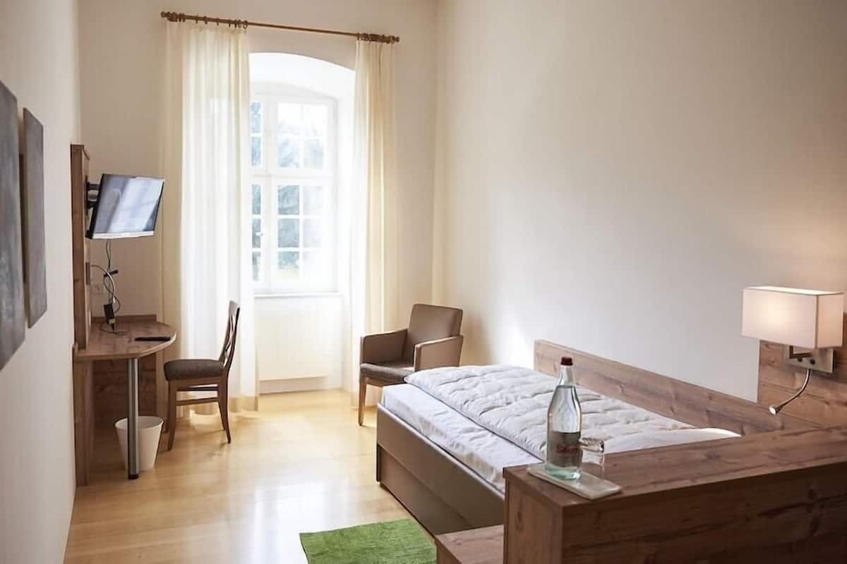 A hotel room with a bed, desk, chair, and a television.
