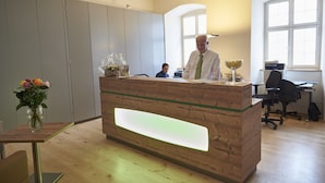 A reception desk with a wooden finish and a glass panel, a vase with flowers, and a desk lamp. - Klosterhotel Kreuz (Metzerlen)