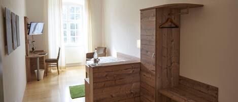 A room with a wooden wardrobe, a desk with a chair, a bed, and a window with curtains.