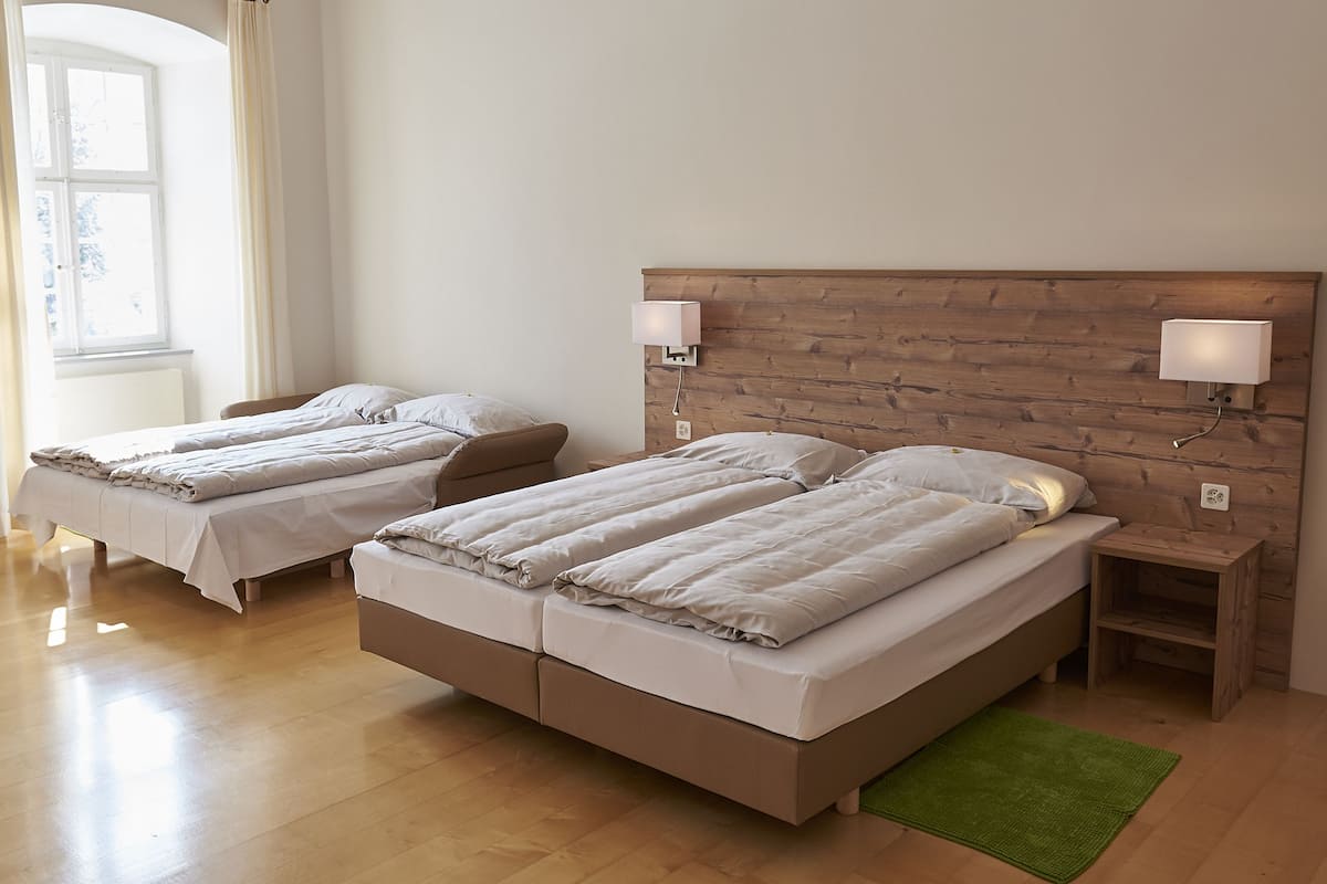 A hotel room with two single beds, wooden headboards, bedside lamps, and a green rug.